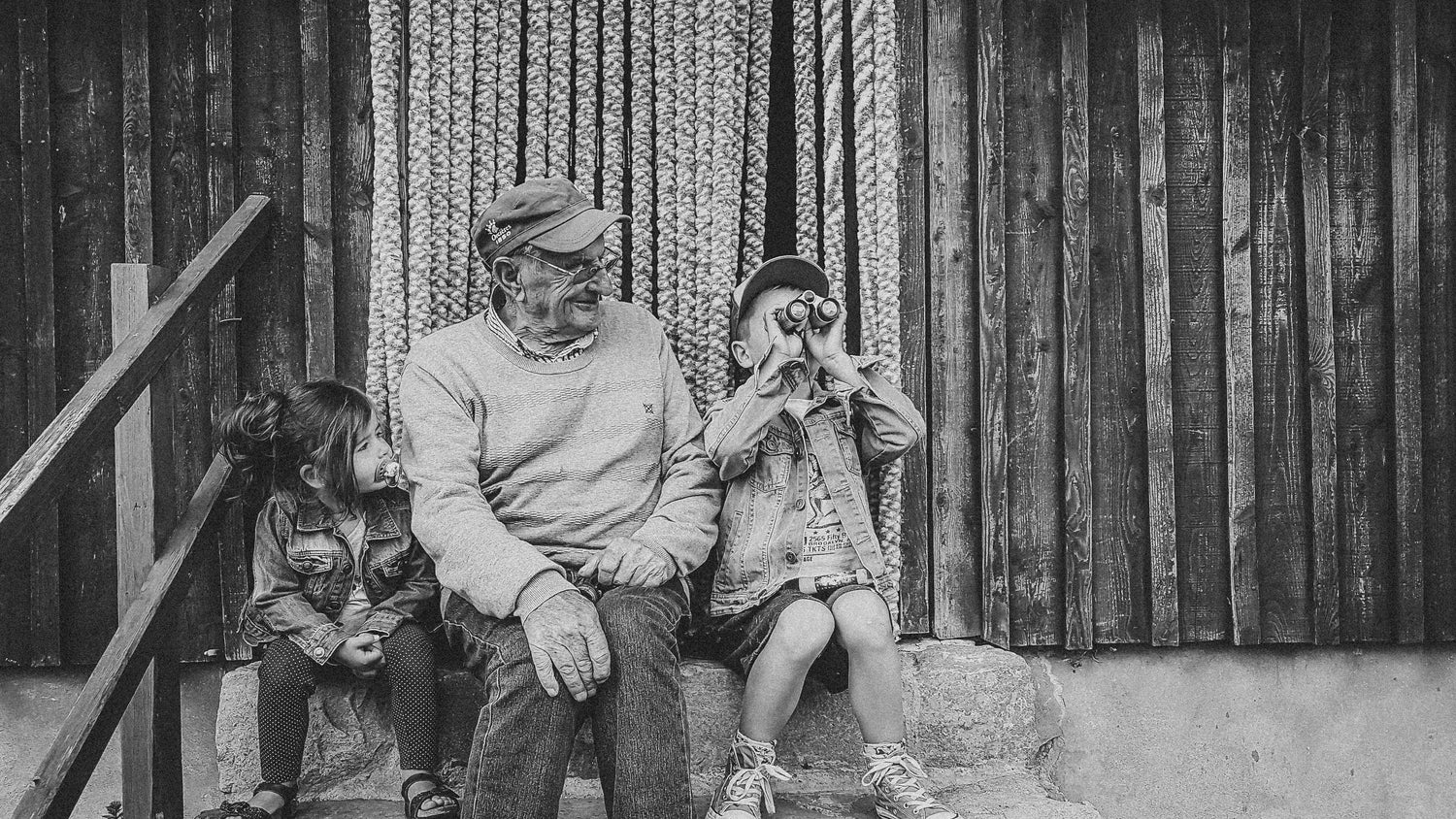 Photo en noir et blanc de Joujou, fondateur de la recette originale du génépi Guillaumette, assis devant un chalet avec ses petits-enfants