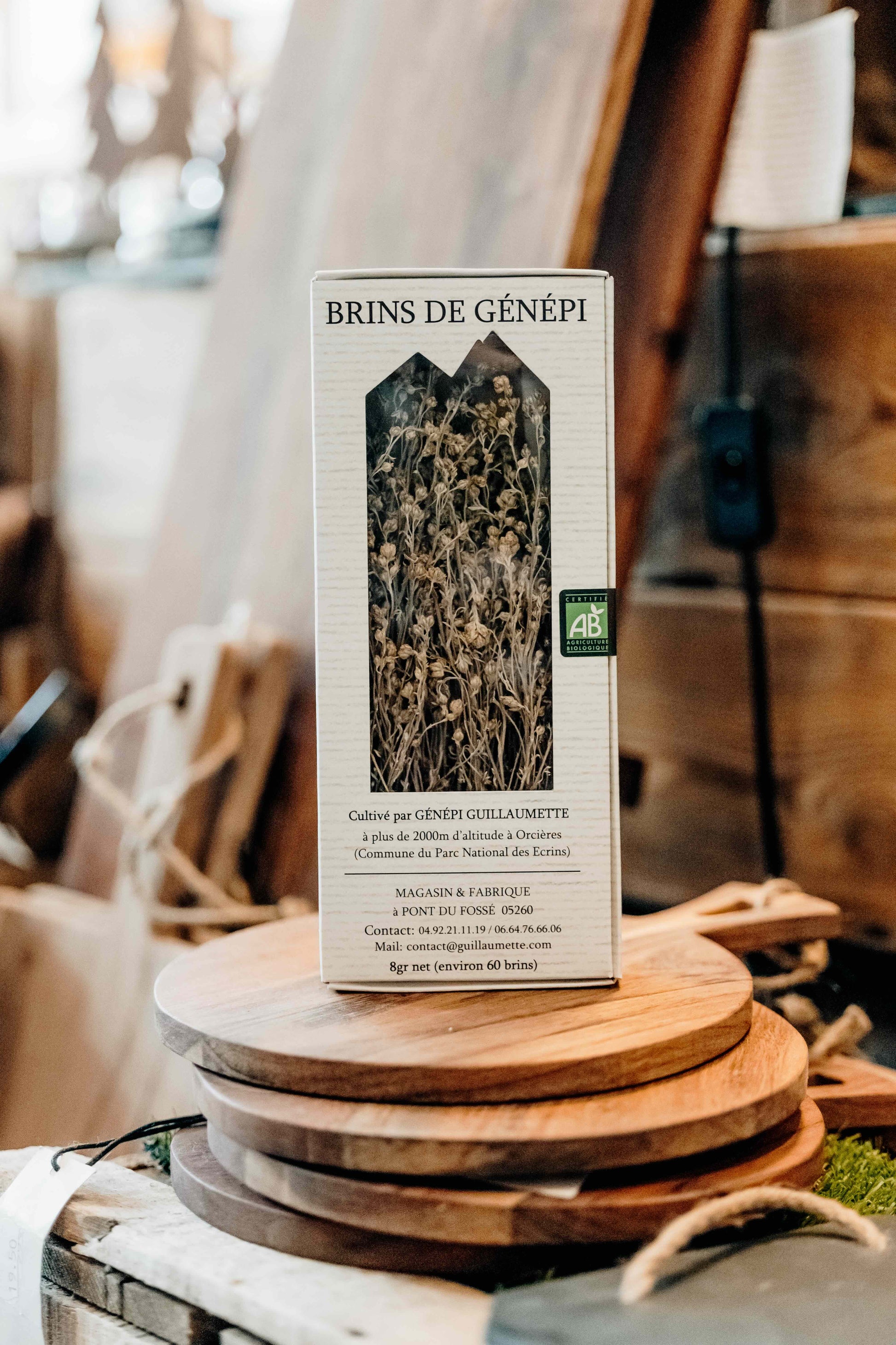 Boîte de brins de génépi bio Guillaumette posée sur des planches en bois dans un décor artisanal