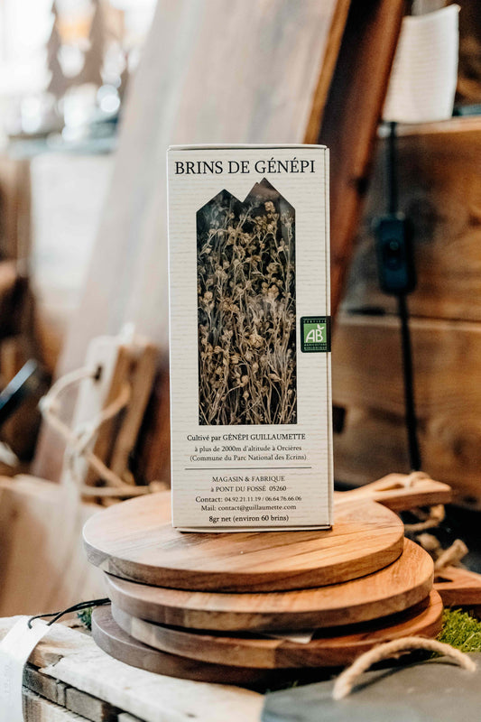 Boîte de brins de génépi bio Guillaumette posée sur des planches en bois dans un décor artisanal