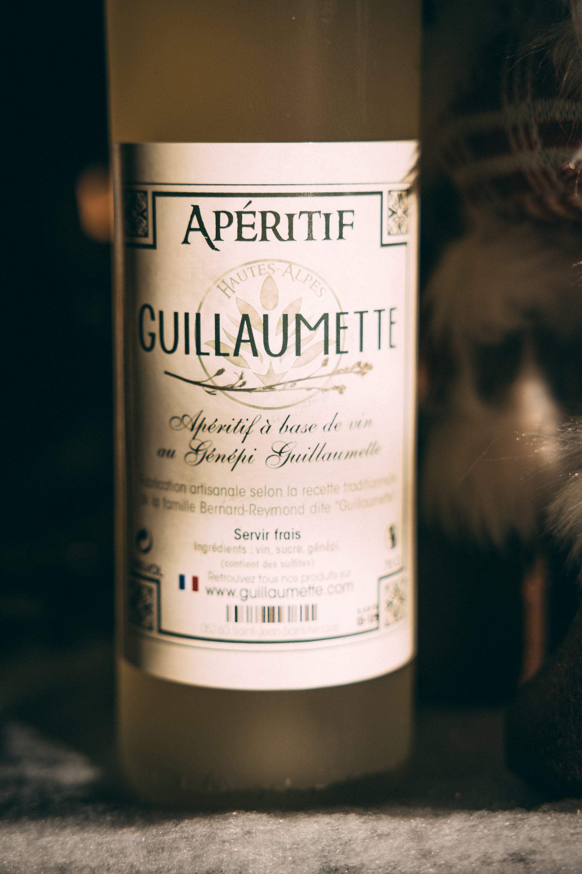 Gros plan sur l’étiquette d’une bouteille de Guillaumette, apéritif artisanal à base de vin au génépi, fabriqué selon la recette traditionnelle de la famille Bernard-Reymond dans les Hautes-Alpes.